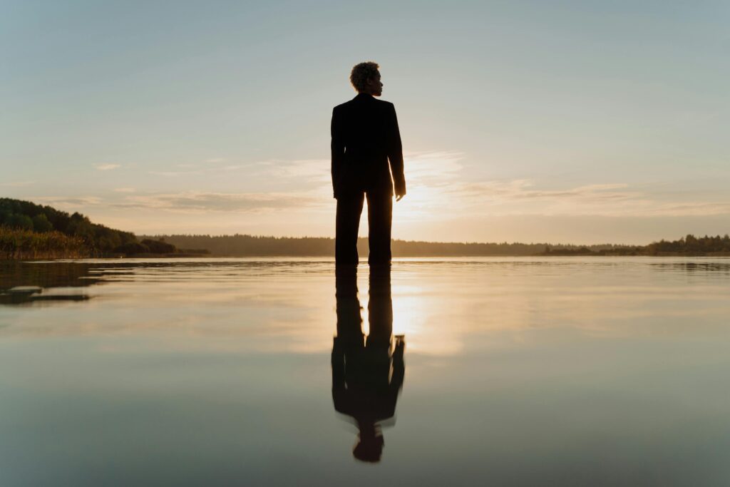 Dramatic silhouette of a man in a suit standing on water at sunset, reflected on calm surface.